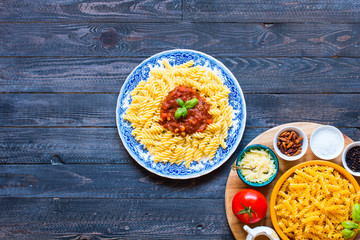 Fusilli pasta with tomato sauce, tomatoes, onion, garlic, dried paprika, olives, pepper and olive oil, on a wooden background.