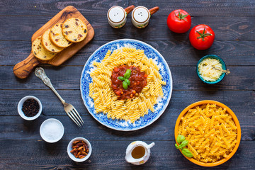 Fusilli pasta with tomato sauce, tomatoes, onion, garlic, dried paprika, olives, pepper and olive oil, on a wooden background.
