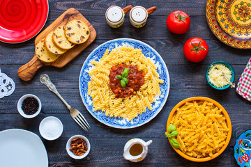 Fusilli pasta with tomato sauce, tomatoes, onion, garlic, dried paprika, olives, pepper and olive oil, on a wooden background.