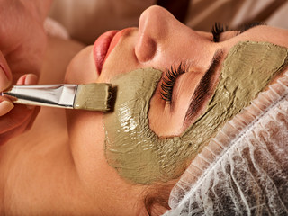 Mud facial mask of woman in spa salon. Massage with clay full face. Girl on with therapy room. Beautician with brush therapeutic procedure . Unique properties of therapeutic clay .