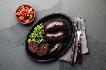 Bloody sausages, chilean prieta on cast iron plate with tomato sauce. Slate background, top view
