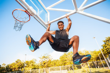 Fototapeta premium Basketball player hangs on the rim.attractive,laugh,sport games,street ball,black,sport outfit,casual wear,black clothes