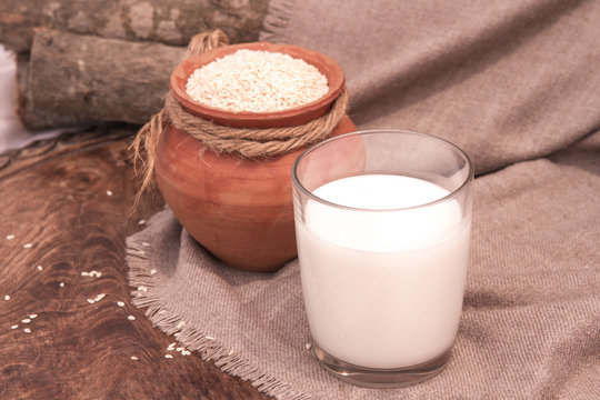 Sesame milk in glass and sesame seed in clay pot on a wooden table.