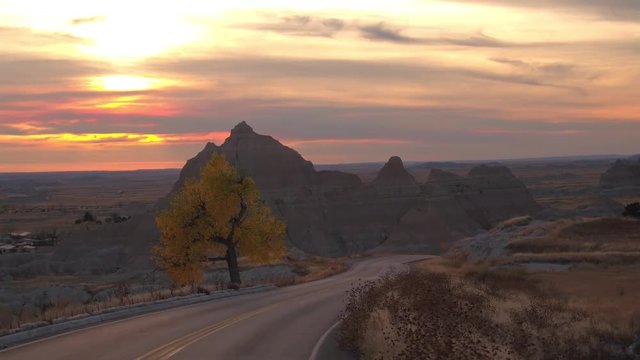 Amazing sunset sky behind the rocky sandstone formations in Badlands National Park. Winding road through Badlands grassland desert in South Dakota at reddish sunrise. Road trip across United States
