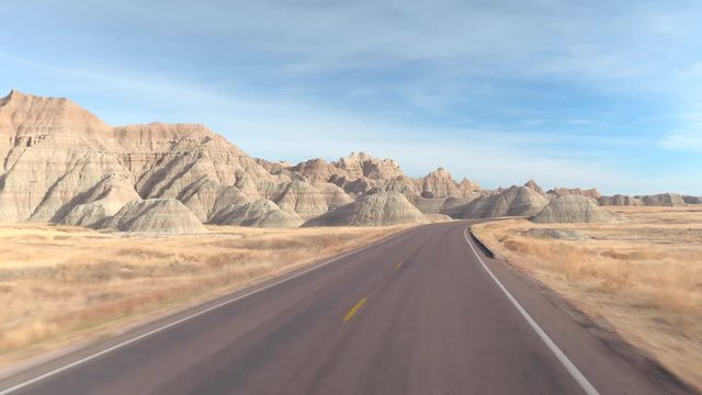 FPV: Driving along the empty road winding past amazing Badlands landscape with rocky sandstone mountains. Traveling through Badlands grassland desert in South Dakota. Road trip across United States