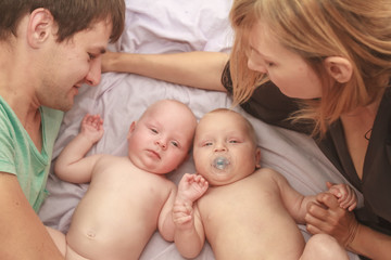 indoor portrait of young happy smiling mother and father with twin babies at home