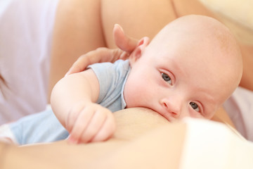 indoor portrait of mother breast feeding and hugging her baby, at home