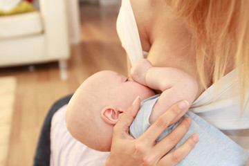 indoor portrait of mother breast feeding and hugging her baby, at home