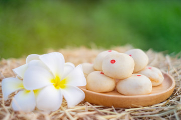 Mochi snacks are placed on wooden boards on straw ground and white flowers are placed on the side. Copy space and blur green background.