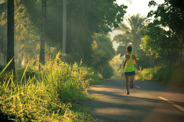 Young fitness woman running on morning tropical forest trail
