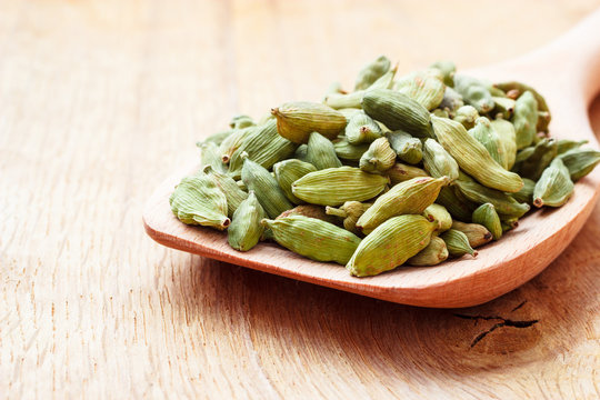 Green cardamom pods on wooden spoon