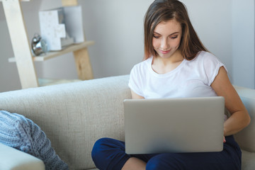 young woman sitting with laptop on sofa at her home