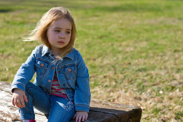 Beautiful charming little girl in jeans with disheveled hair on a background of green