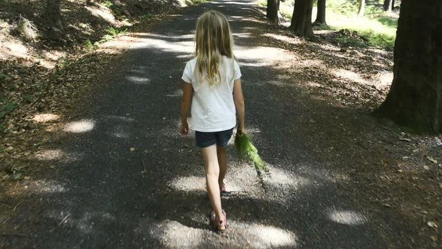 A child girl walking barefoot on a forest mountain road in bright summer light. Handheld smooth footage