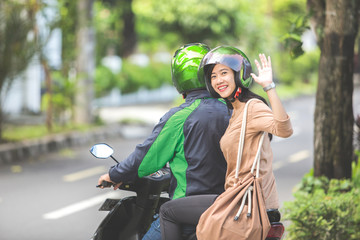 passenger waving good bye while sitting on a commercial motorcycle taxi