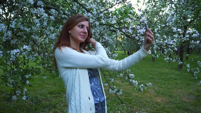 Young beautiful girl makes selfie on phone in a blooming Apple orchard.