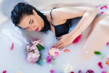 Obraz na płótnie Canvas Sexy brunette woman lying on one side in a hot bath with flowers. she is wearing black sexual lingerie. woman in bath