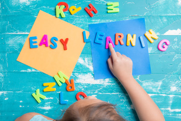 Children play plastic letters to combinations word "Easy Learning" on wood table.