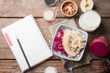 Bowl of oatmeal porridge with bananas, apple, dragon fruit and almonds. Top view