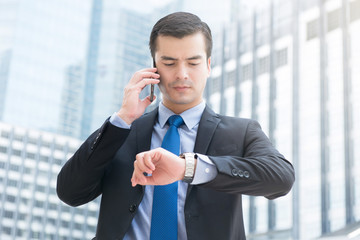 Businessman looking at his watch checking time while calling on cell phone