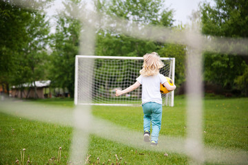 Fototapeta na wymiar Little boy with long blond hair playing football on football pitch