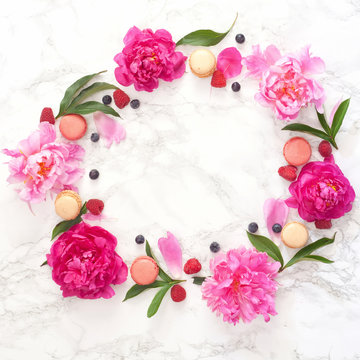 Flat lay frame with pink and white peonies, berries, macarons, leaves and petals. Top view
