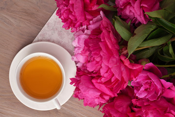 Tea time. Flat lay over wooden background with peonies, macaroons and cup of tea
