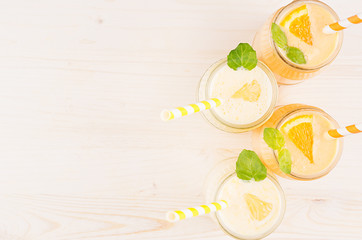 Freshly blended orange and yellow lemon smoothie in glass jars with straw, mint leaf, top view. White wooden board background, copy space.