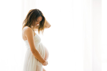 Portrait of young pregnant attractive woman, standing by the window,