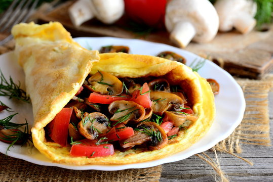 Golden omelette with vegetarian filling. Healthy omelette with fried mushrooms, fresh tomatoes and dill on a plate. Closeup