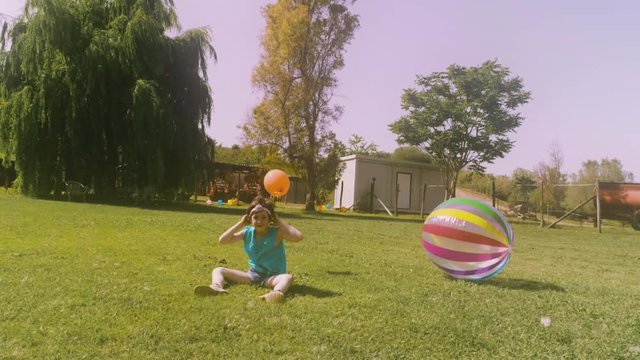 Cute little girl puts headband and playing with big coloroful ball at the countryside