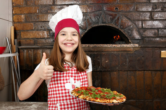 happy little girl cook with pizza and thumb up in pizzeria