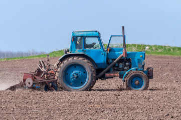 Fototapeta premium An old tractor in the field plows the land. Spring landscape of a countryside, a farm.