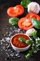 Tomato ketchup sauce in a bowl with spices, basil leaves and tomatoes on the kitchen table.