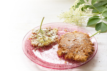 fried elderflower pancakes with icing sugar on a pink glass dish