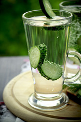 Cold drinking water in a glass with a cucumber on a wooden board