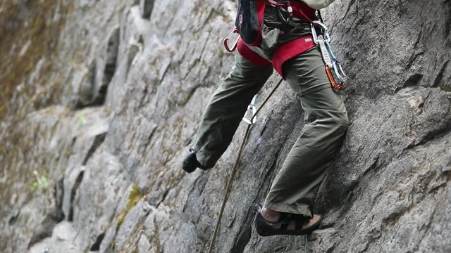 Detail of strong healthy young rock climbing man, legs and feet. Climber steps left and then up. Security harness, rope and quickdraw. Slow motion at 120 fps. Patagonia Argentina.