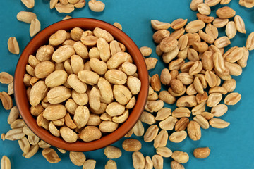 Roasted salted peanuts in bowl  on blue background, top view