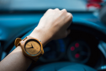business woman hand wearing wooden wrist watch. her holding steering wheel car for driving and have...