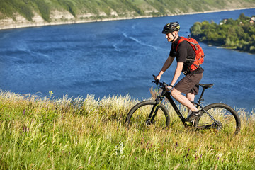 Obraz premium Attractive cyclist riding the mountain bicyclist on the summer trail above the river.