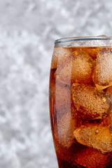 Cola in glass with ice cubes on black and white concrete background
