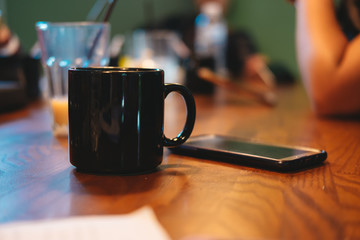 coffee cup put beside mobile phone. all of this putting on wooden table in meeting room and have group of business are background. 