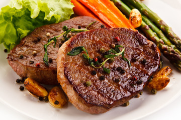Grilled beef steaks with asparagus and carrots on white background 