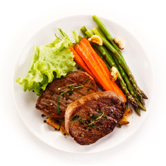 Grilled beef steaks with asparagus and carrots on white background 