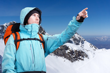 The mountaineer pointing at peak, standing against a winter mountain landscape.