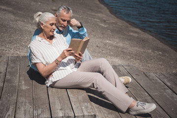 elderly couple reading book while resting on the quay at daytime