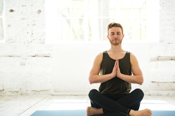 Young smiling guy sitting on a fitness mat and meditating