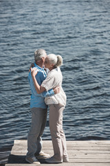 Fototapeta na wymiar casual grey haired couple hugging on riverside at daytime