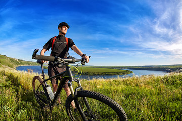 Attractive mountain cyclist stands on the hill above the beautiful river.