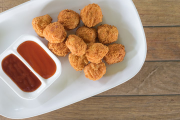 chicken nuggets putting in dish. have small cup with chilli sauce and tomato sauce all of it putting on wooden table are background. this image for food concept